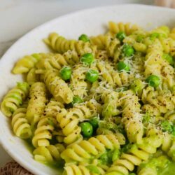 Pasta with green peas and grated cheese on a white plate, creamy and flavorful Alfredo sauce, served warm.