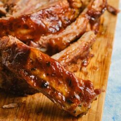 Juicy grilled pork ribs with barbecue sauce on a wooden cutting board.
