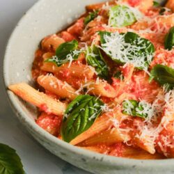 Pasta with tomato sauce, basil, and Parmesan cheese in a white ceramic bowl.