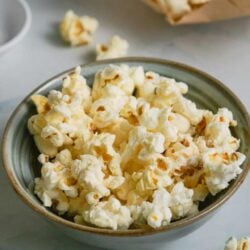 Buttered popcorn in a bowl with scattered popcorn pieces on table, snack food, movie night, close-up.