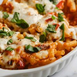 Baked ziti pasta casserole with melted cheese, fresh basil, and tomato sauce in a white baking dish.
