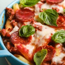 Savory pepperoni and beef baked ziti with melted cheese and fresh basil in blue casserole dish.
