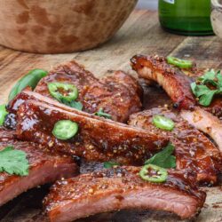 Succulent BBQ pork ribs glazed with sauce, garnished with fresh herbs and green onions on a rustic wooden cutting board.