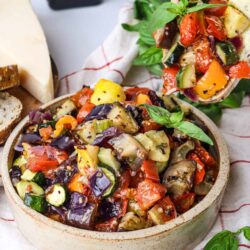 Roasted vegetable caponata served in a bowl and on bread, made with eggplant, zucchini, tomatoes, and herbs for a flavorful vegan appetizer.