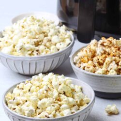Buttered popcorn in bowls with a popcorn machine in the background.