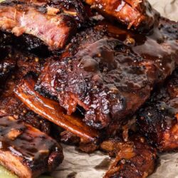Succulent slow-cooked barbecue ribs glazed with rich, smoky sauce, served with pickle spears on parchment paper.