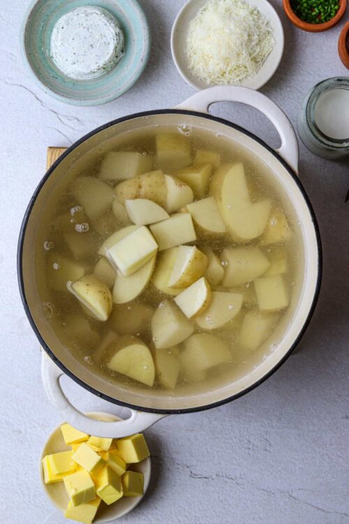 Boiled potatoes in a white pot with baking ingredients around.