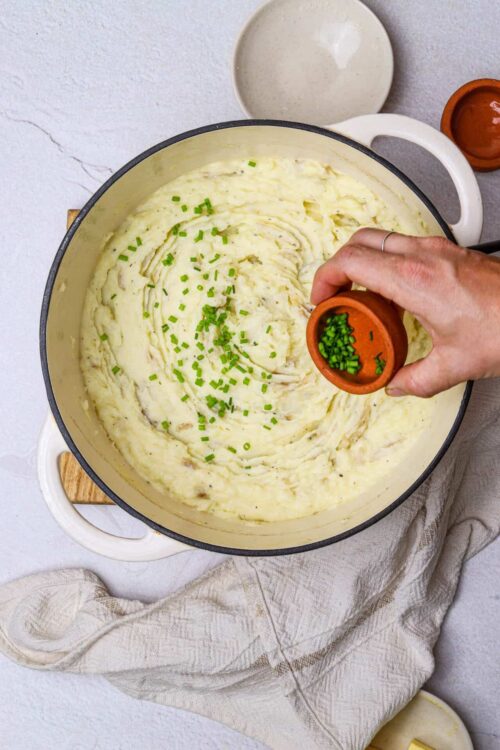 Creamy mashed potatoes with chopped chives being prepared in a pot.