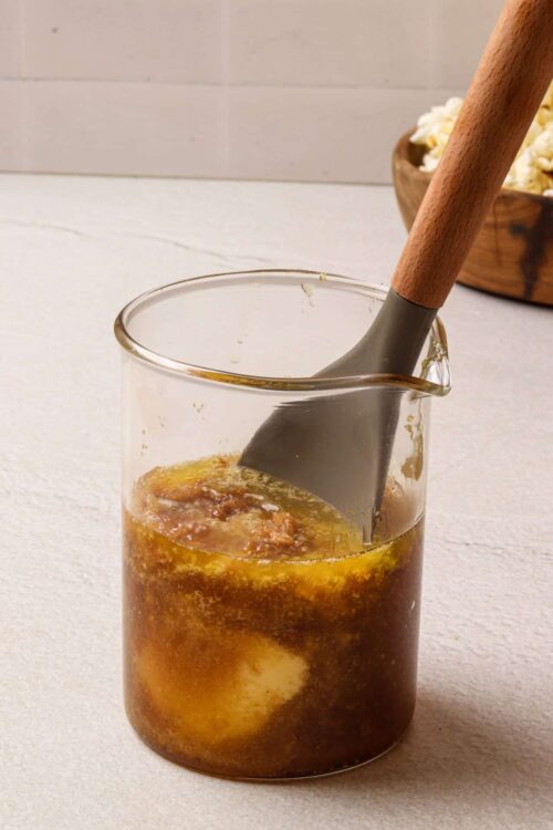 Homemade caramel sauce in a glass jar with a spatula, ready to pour.