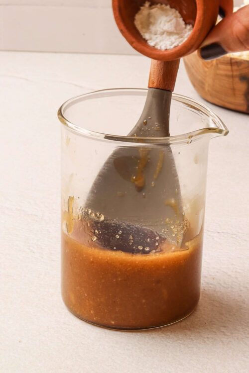 Rich caramel sauce being stirred in a glass mixing jug with a wooden spoon.
