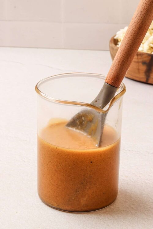 Creamy caramel sauce in a glass jar with a wooden-handled spatula. Perfect for desserts and baking.