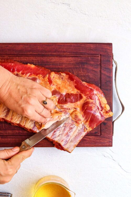 Smoked pork ribs being sliced on a wooden cutting board for BBQ.