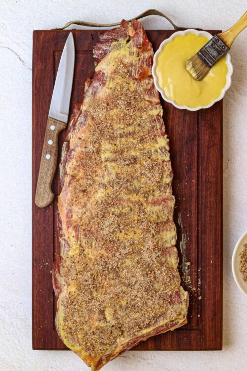 Juicy baked pork ribs with seasoned coating on wooden cutting board.