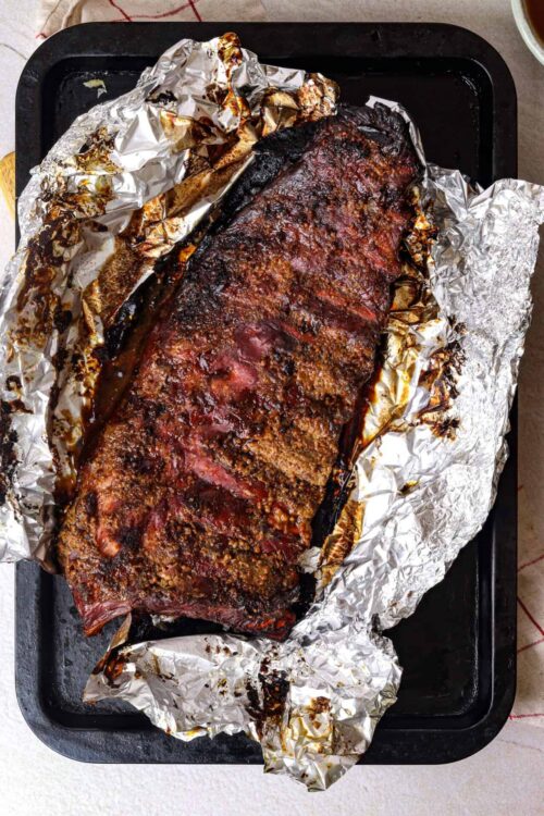 Juicy, perfectly smoked beef brisket with savory bark, wrapped in aluminum foil on a baking sheet.