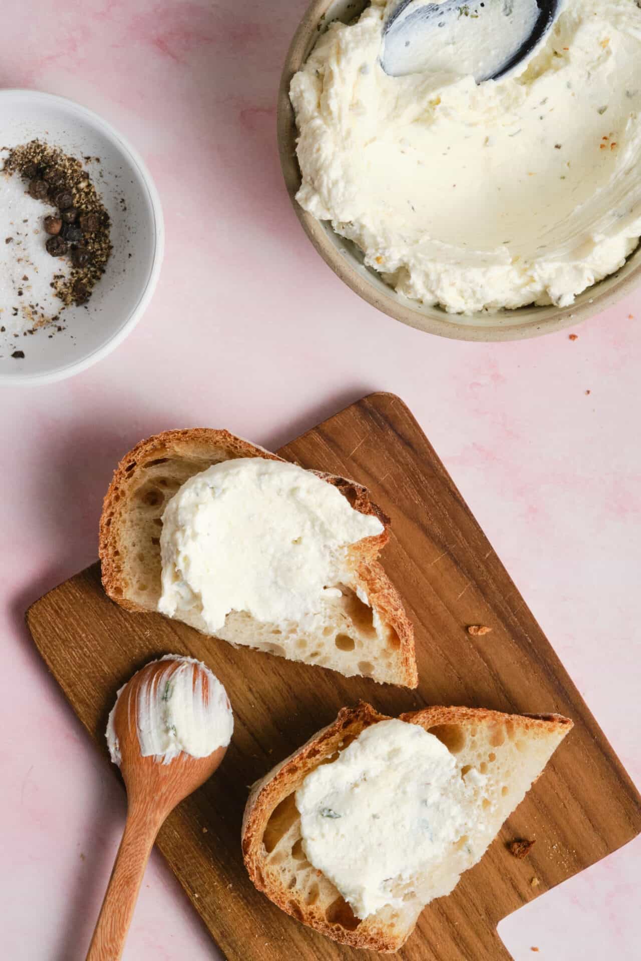 Cream cheese spread on sliced baguette bread with black pepper and salt in the background.