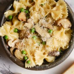 Creamy mushroom and pea pasta in a rustic black skillet, topped with cheese and fresh herbs.