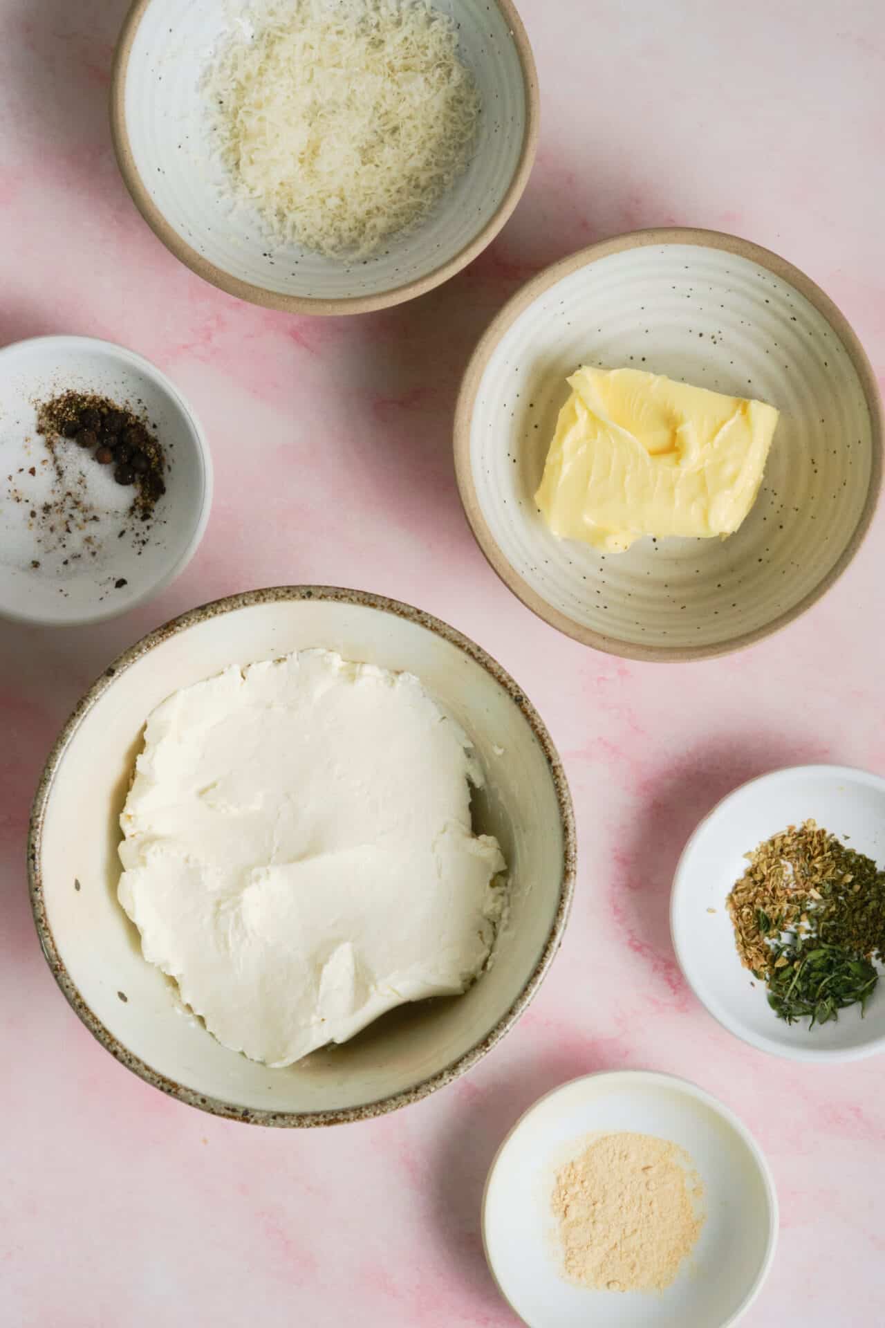 Cream cheese, butter, and seasonings on a pink background for baking.