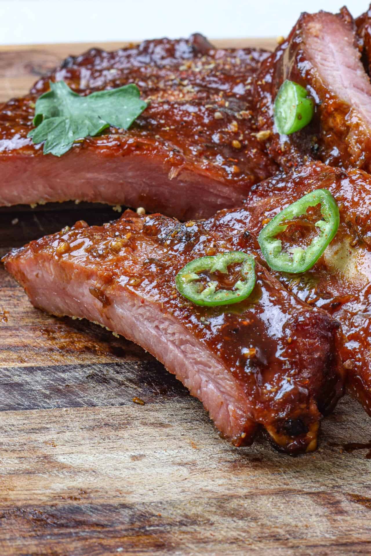 Juicy glazed pork ribs with green chili slices on wooden cutting board.