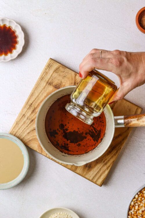 Soy sauce being poured into a bowl on a wooden cutting board, surrounded by dipping sauces and ingredients.