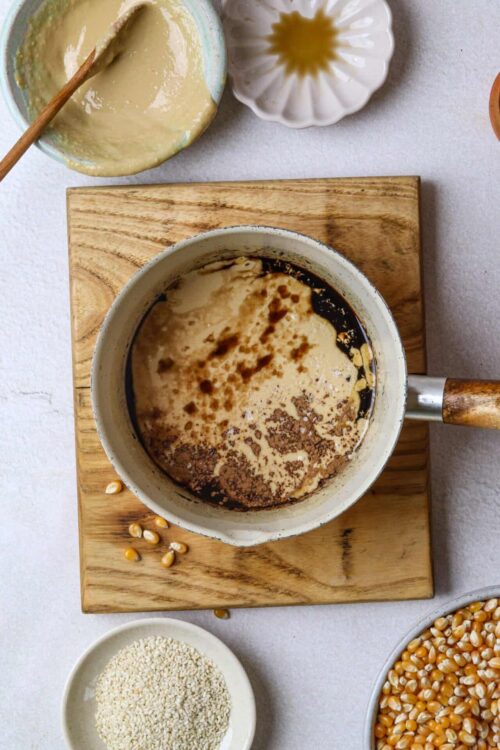 Creamy baking ingredients with vanilla bean, corn, and sesame on a rustic wooden board.