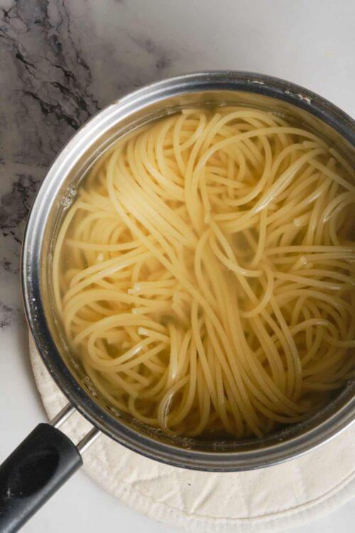 Cooked spaghetti pasta submerged in water in a stainless steel pot.