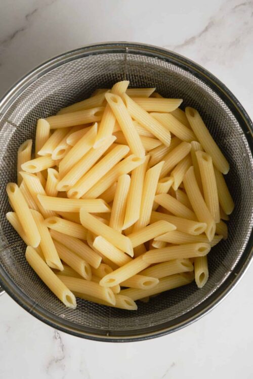 Cooked penne pasta in a stainless steel strainer for easy draining.