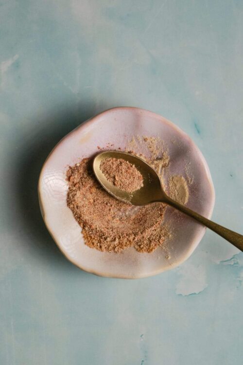 Ground cinnamon in a small dish with a spoon on a pastel surface, perfect for baking recipes.