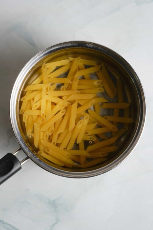 Cooked penne pasta in a stainless steel saucepan, ready for recipes or meal preparation.