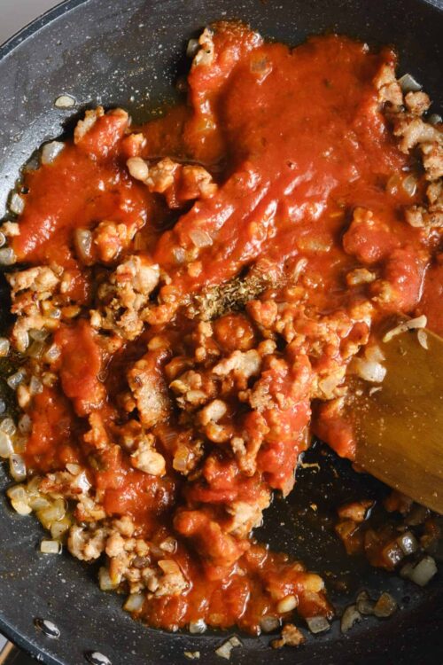 Ground beef cooking with tomato sauce and onions in a skillet, delicious and savory meal.