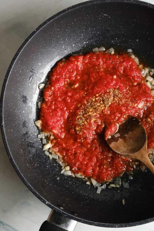 Simmering tomato sauce in a black skillet with garlic and crushed red pepper flakes.