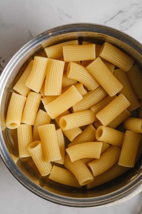 Golden rigatoni pasta in stainless steel pot ready for cooking.