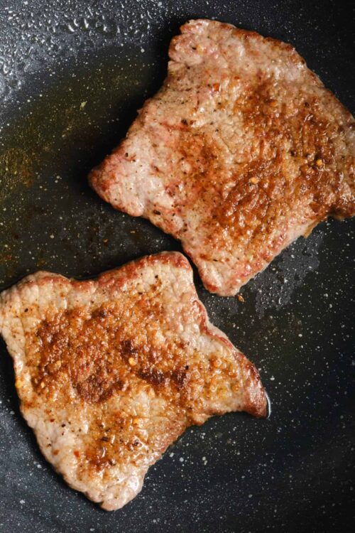 Juicy, seasoned pork chops sizzling in a black skillet with golden-brown crust.