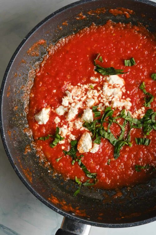 Savory tomato and cheese sauce in a black skillet with chopped basil.