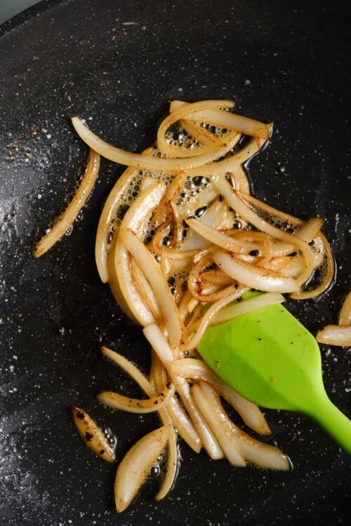 Sauteed onions cooking in a black skillet with a green spatula for caramelized flavor.