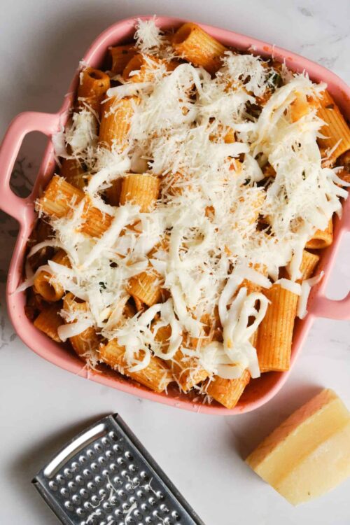 Pasta baked with cheese in pink baking dish, grated Parmesan and shredded mozzarella cheese on top.