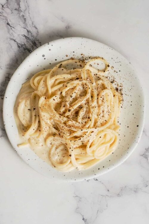 Creamy garlic Alfredo pasta on white plate with black pepper, close-up.