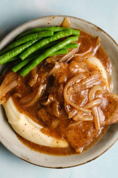 Juicy chicken with gravy, mashed potatoes, and green beans on a rustic plate.