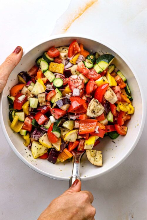 Freshly chopped colorful vegetable salad in a white bowl with a serving spoon.