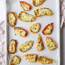 Roasted stuffed bell peppers with cheesy filling on baking sheet, healthy baked vegetable appetizer.