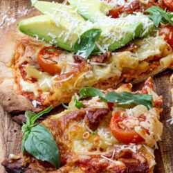 Pizza with avocado, cheese, and fresh basil on a rustic wooden board.