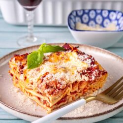 Hearty homemade lasagna with melted cheese, rich tomato sauce, and fresh basil on a rustic plate.