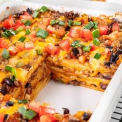 Cheesy beef enchiladas topped with fresh tomatoes and green onions in a baking dish.