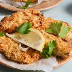 Crispy baked fish fillets with lemon and herbs on a plate with parsley.