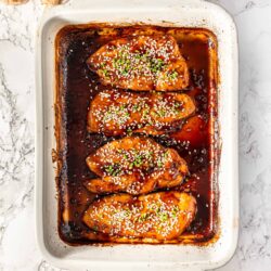 Savory baked chicken thighs in rich, glazed sauce garnished with sesame seeds and chopped green onions.