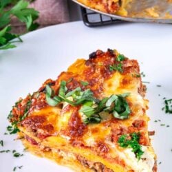 Savory homemade lasagna on white plate with fresh herbs, baked to perfection.