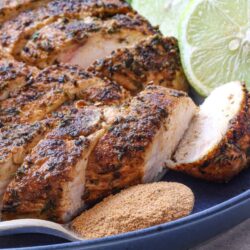Roasted herb chicken with lime slices on black platter.