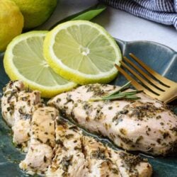 Juicy herb-marinated chicken breast with lemon slices on a blue plate.