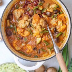 Hearty vegetable and bean stew with cauliflower, mushrooms, and green onions served in a white pot.