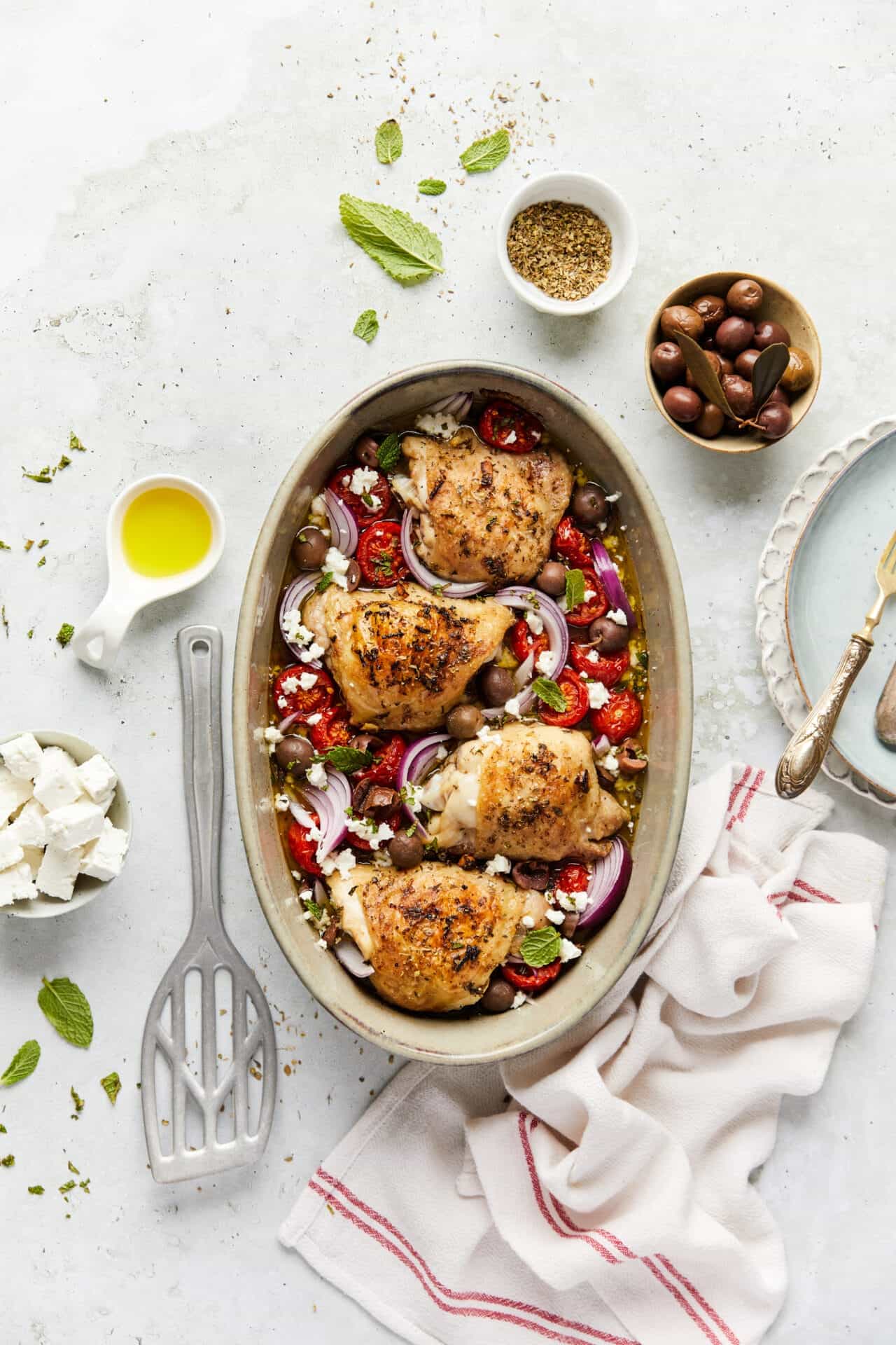 Juicy baked chicken thighs with tomatoes, olives, and herbs on a white serving dish.