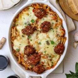 Savory baked ziti with meatballs, melted cheese, and fresh herbs in a white casserole dish.